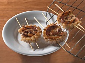 Three grilled pork belly skewers on plate and grill