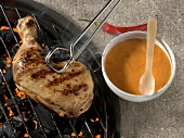 Chicken legs on grill with tongs and bowl of marinade