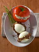 Stuffed tomato and two eggs filled with pumpernickel kruste on plate