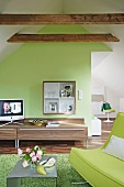 Room with green sofa, table, sideboard, television, sloping ceiling and roof beam