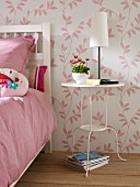 White-painted metal side table next to bed in bedroom with pink and white floral wallpaper