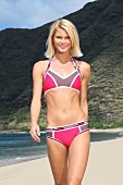 Portrait of attractive blonde woman wearing sports bikini, standing on beach and smiling