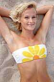 Pretty blonde woman wearing tube top bikini lying on beach, smiling