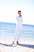 Frau am Strand trägt weiße Strickjacke und weiße Hose