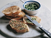 Slices of roasted white bread and bowl of garlic and parsley dip