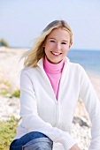 Blonde Frau trägt weiße Jacke und rosa Rollkragen-Shirt
