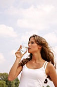 Frau in weißem Top trinkt Wassser aus einem Glas