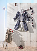 Floral print short coat, shorts and scarf hanging on wooden wall with red shoes on sand