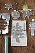 Christmas tree decorations cut out of silver paper on wooden surface
