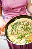 Mensch hält Pfanne mit Omelett mit Schnittlauch in den Händen