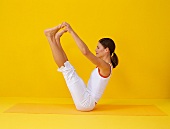 Pilates - Open Leg Rocker: Frau sitzt, Beine oben, Hände an Zehe