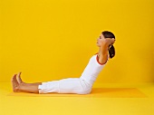 Pilates - Neck Pull: Frau sitzt, zurücklehnen, Rücken u. Beine gerade