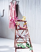 Various shoes arranged on ladder with pink dress on hanger in background