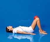 Side view of woman in supine position exercising with ball between her knees 