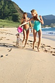 Zwei Frauen laufen spielend mit einem Hund am Strand entlang