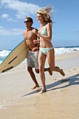 Man and woman running with a surfboard on the beach