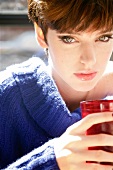 Portrait of green eyed woman with short hair in blue sweater holding red glass with drink