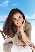 Portrait of pretty woman in gray sweater and white pants sitting on beach, smiling