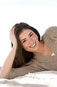 Portrait of happy woman wearing beige sweater lying with head propped on hand, smiling