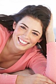 Portrait of pretty woman wearing pink sweater lying on sand with hand on head, smiling