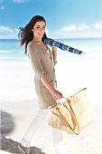 Pretty woman holding umbrella and handbag walking on beach, laughing
