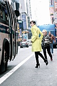 Woman wearing long coat and high heels walking on street along bus, looking over shoulder