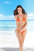 Beautiful woman in orange bikini walking on beach, smiling