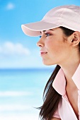 Side view of pretty woman with long brown hair wearing pink cap on beach, close-up