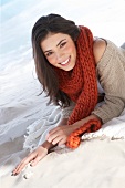 Portrait of beautiful woman wearing red scarf and beige cardigan lying on beach, smiling