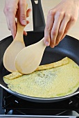 Omelette being rolled up with two flat wooden spoon in frying pan, step 1
