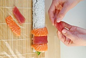 Placing slices of fish on rice while preparing rainbow sushi on sushi mat, step 3