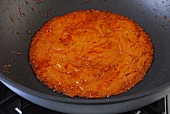 Brown mixture of coconut milk being boiled in pan while preparing Thai curry, step 3