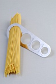Raw spaghetti in pasta portioning tool on white background