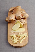 Pieces, strips slices and whole ginger root on wooden cutting board