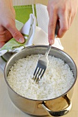 Rice being loosened with fork in casserole, step 4