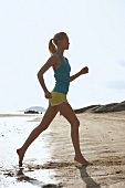 Side view of blonde woman wearing sportswear jogging on beach