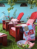 Rote Holzsessel im Garten mit gemusterten Kissen und Decken