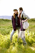 Two pretty women wearing knitted clothes walking through meadows on hills