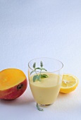 Mango lassi with mint in glass lemon wedge and halved peach on white background