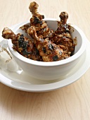 Bowl of chicken drumsticks with plum and mustard glaze in serving dish
