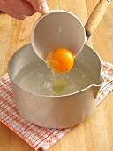 Egg yolk being added into water in sauce pan, step 1