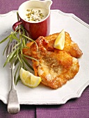 Fried fish with tartar sauce, lemon wedges and savoury on plate