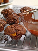 Chocolate muffins with orange segments and bowl of chocolate icing on oven grill