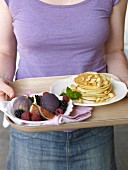 A woman holding a tray of pancakes and a fruit platter