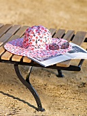 Pink floral pattern sun hat and glasses on wooden bench