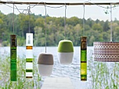 Six lanterns made of felt and glass hanging on wooden stick with lake in background