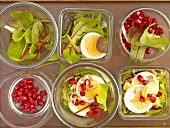 Six bowls of salad with eggs, pomegranate seeds and leaves