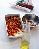 Salami with tomato sauce in casserole and olive oil in bottle