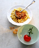 Fusilli with lamb and apricot sauce in serving dish beside tomato in bowl