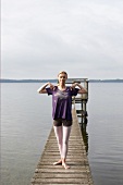 Woman in sportswear pressing her shoulder lightly while exercising on jetty